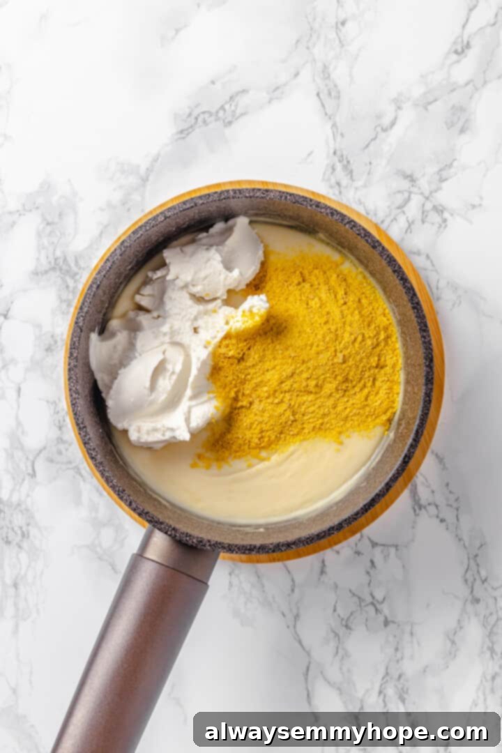 Nutritional yeast and cream cheese being added to the bechamel sauce in a saucepan
