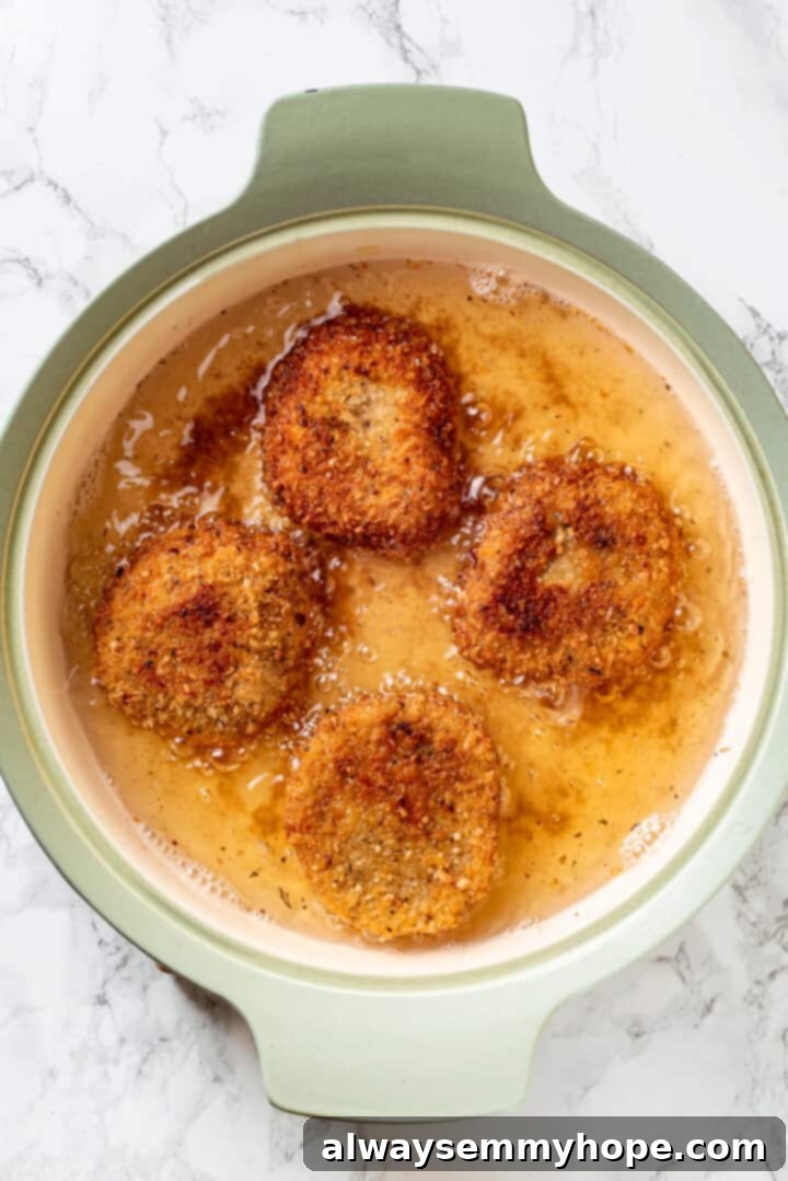 Overhead view of vegan chicken cutlets frying to a golden crisp in hot oil within a large skillet, ready for the next step of the parm sandwich.