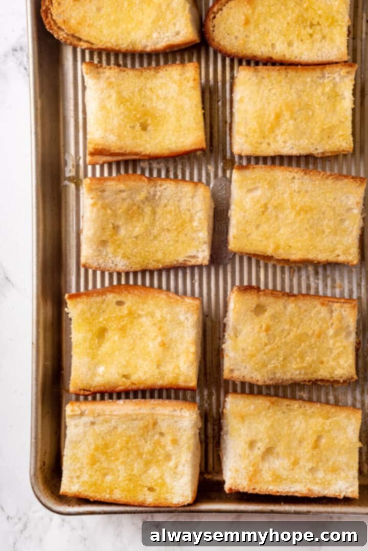 Overhead view of toasted French baguette halves on a baking pan, brushed with olive oil and garlic powder, golden and ready for assembly.