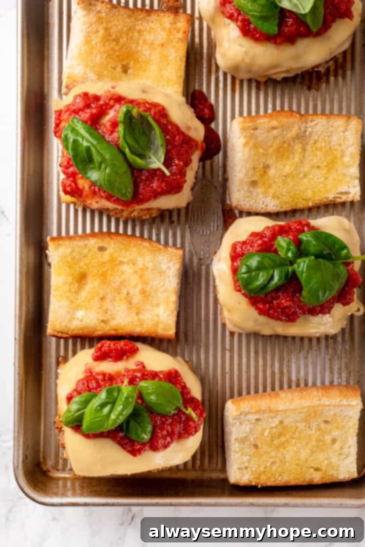 Overhead view of vegan chicken parm sandwiches being meticulously assembled, with melted cheese, marinara, and fresh basil layered onto toasted baguettes.