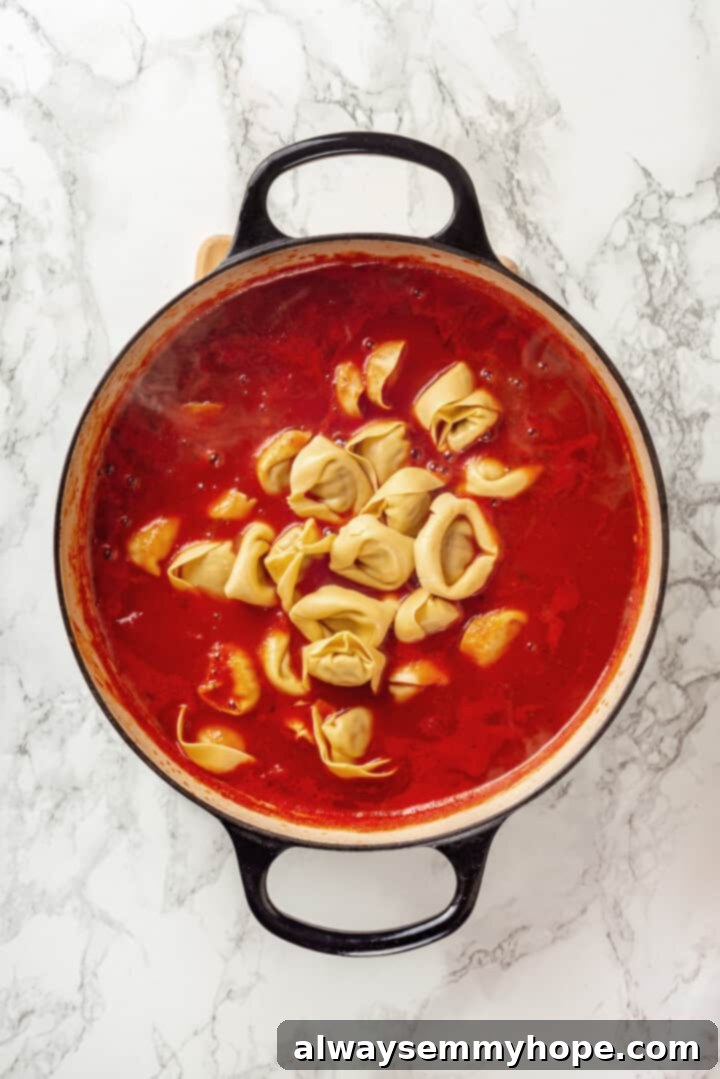 This easy tomato tortellini soup recipe is comfort food in a bowl. You’ll love the creamy tomato broth but the tortellini is the best part! Overhead view of tortellini added to pot