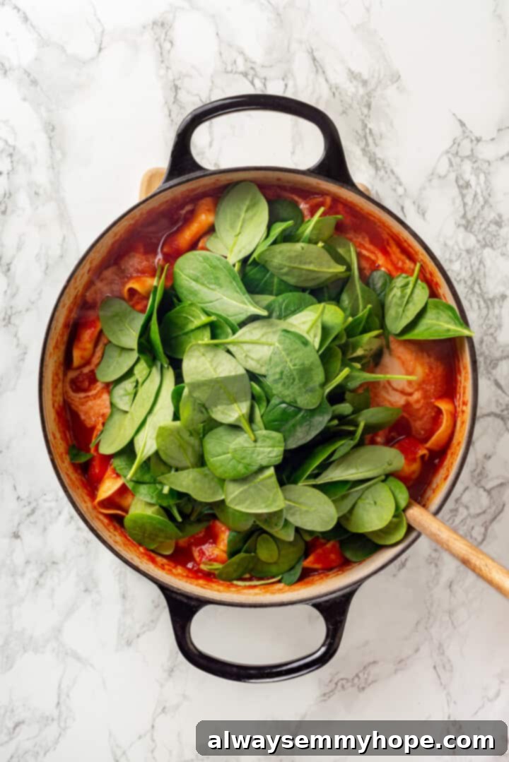 This easy tomato tortellini soup recipe is comfort food in a bowl. You’ll love the creamy tomato broth but the tortellini is the best part! Overhead view of spinach being stirred into tomato tortellini soup