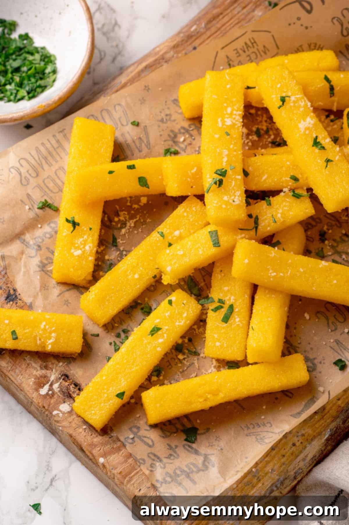 Crispy homemade polenta fries cooling on parchment paper Freshly fried polenta fries resting on parchment paper, with a bowl of green parsley in the soft background