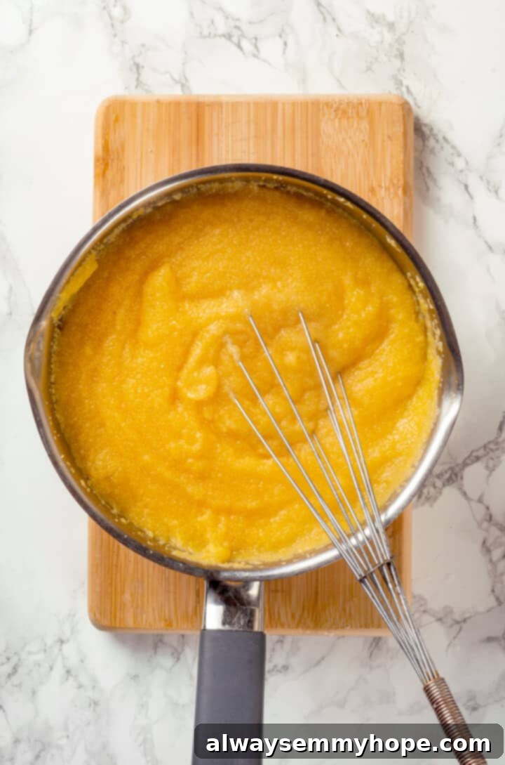 Cooking polenta in a pot for the base of polenta fries Overhead view of creamy polenta being whisked in a saucepan on the stove