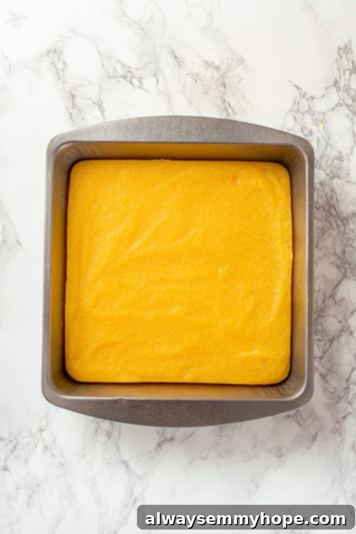 Spreading warm polenta into a greased baking pan for cooling Overhead view of freshly cooked polenta smoothed into an even layer in a baking pan, ready to cool