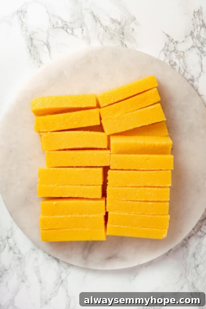 Cutting cooled polenta into fry shapes for frying Overhead view of cooled polenta carefully sliced into uniform strips on a cutting board