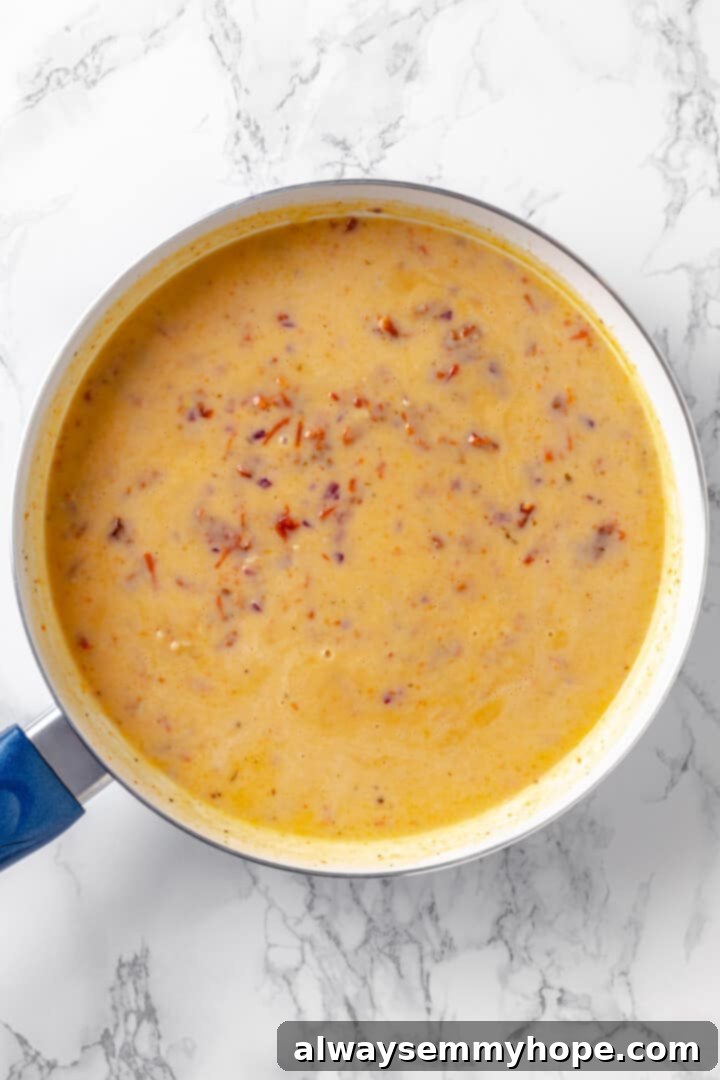 Building a rich, creamy vegan sauce for sun-dried tomato pasta on the stovetop. Close-up overhead view of the creamy vegan sauce for sun-dried tomato pasta simmering in a skillet before spinach is added, showing its rich texture.