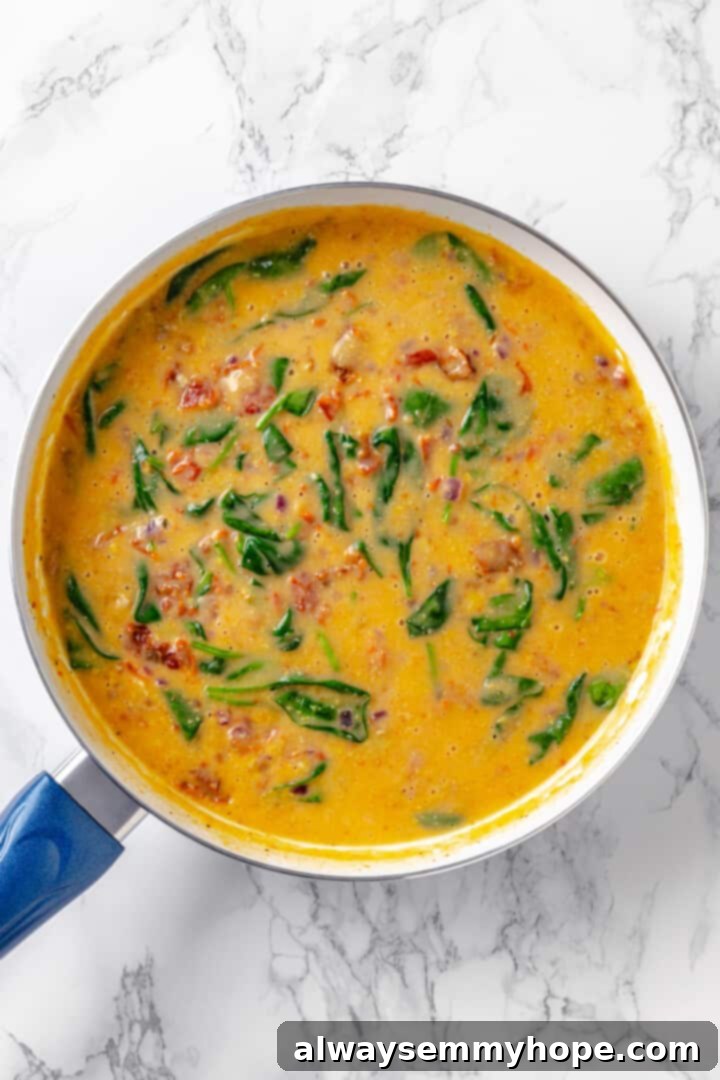 Creamy vegan sun-dried tomato and spinach pasta sauce in a skillet, perfectly wilted. Overhead view of the creamy vegan sauce for sun-dried tomato and spinach pasta, after the spinach has wilted beautifully into the sauce.