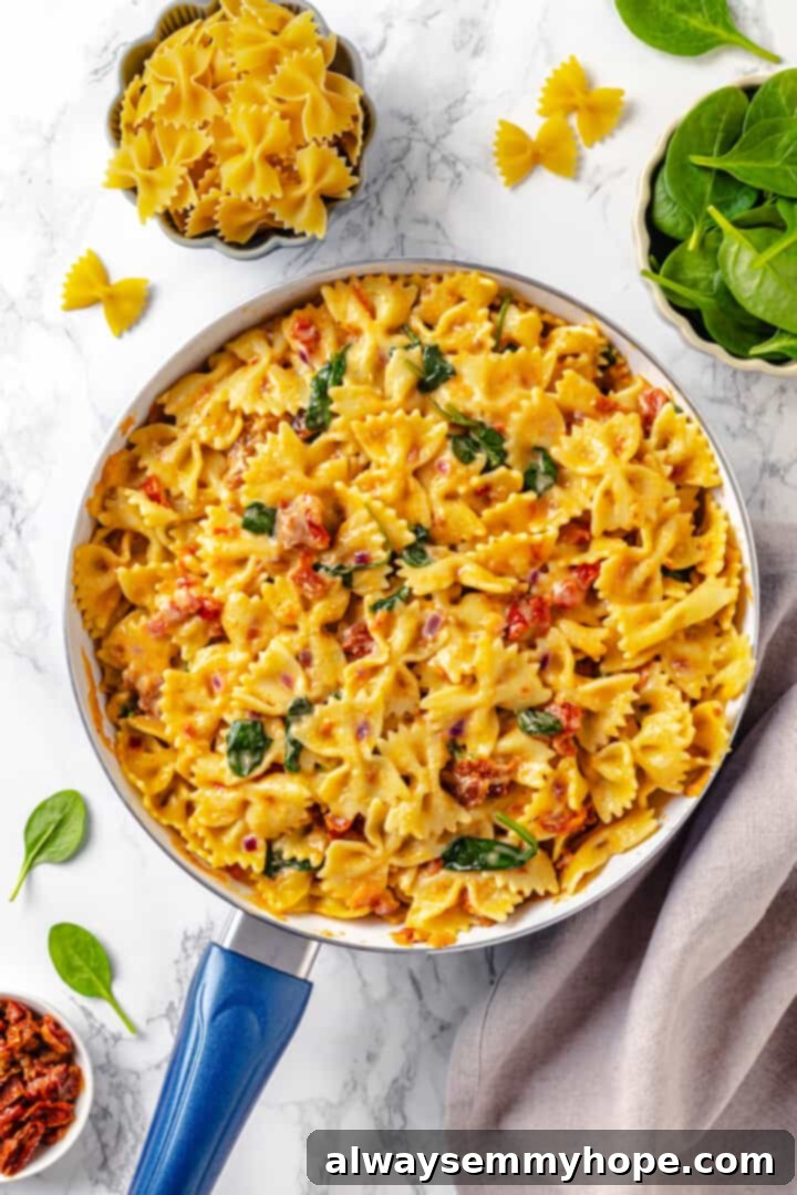 Mixing sun-dried tomato pasta with creamy spinach sauce directly in the skillet. Overhead view of sun-dried tomato pasta mixed with creamy spinach sauce in a large skillet, beautifully coated and ready to be served.