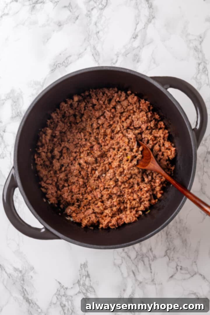 Satisfying cabbage roll soup is a filling meal in a bowl! Skip all the work and enjoy your cabbage rolls in the form of a hearty soup recipe. Overhead view of savory vegan ground beef browning in a pot, being broken up with a wooden spoon.