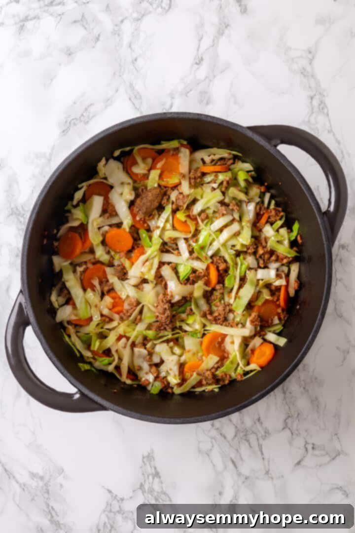 Satisfying cabbage roll soup is a filling meal in a bowl! Skip all the work and enjoy your cabbage rolls in the form of a hearty soup recipe. Overhead view of a vibrant mix of carrots, garlic, and wilted cabbage sautéing alongside vegan beef in a large soup pot.