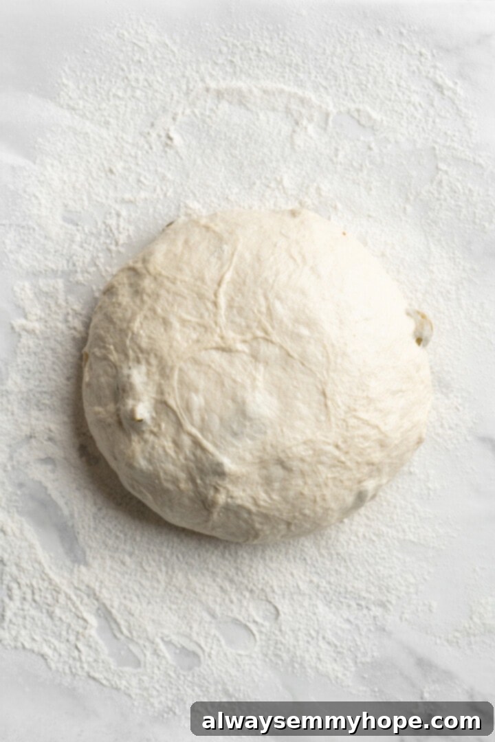 This crusty no-knead olive bread recipe is perfect for beginning bakers, but seasoned pros will love it too. Easy and delicious! Overhead view of shaped dough for olive bread on parchment paper, ready for scoring