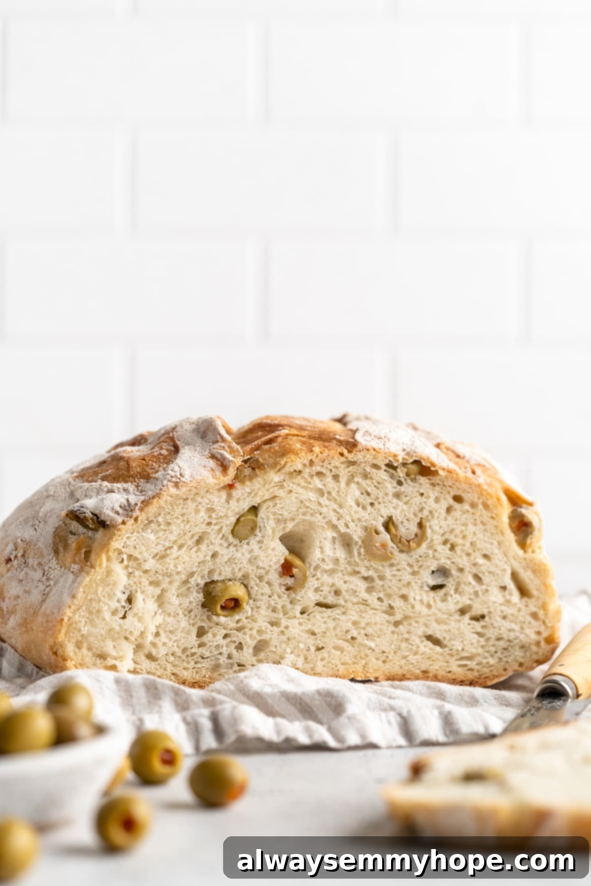 This crusty no-knead olive bread recipe is perfect for beginning bakers, but seasoned pros will love it too. Easy and delicious! Cut olive bread loaf on a cutting board, revealing its soft, olive-studded interior and airy crumb