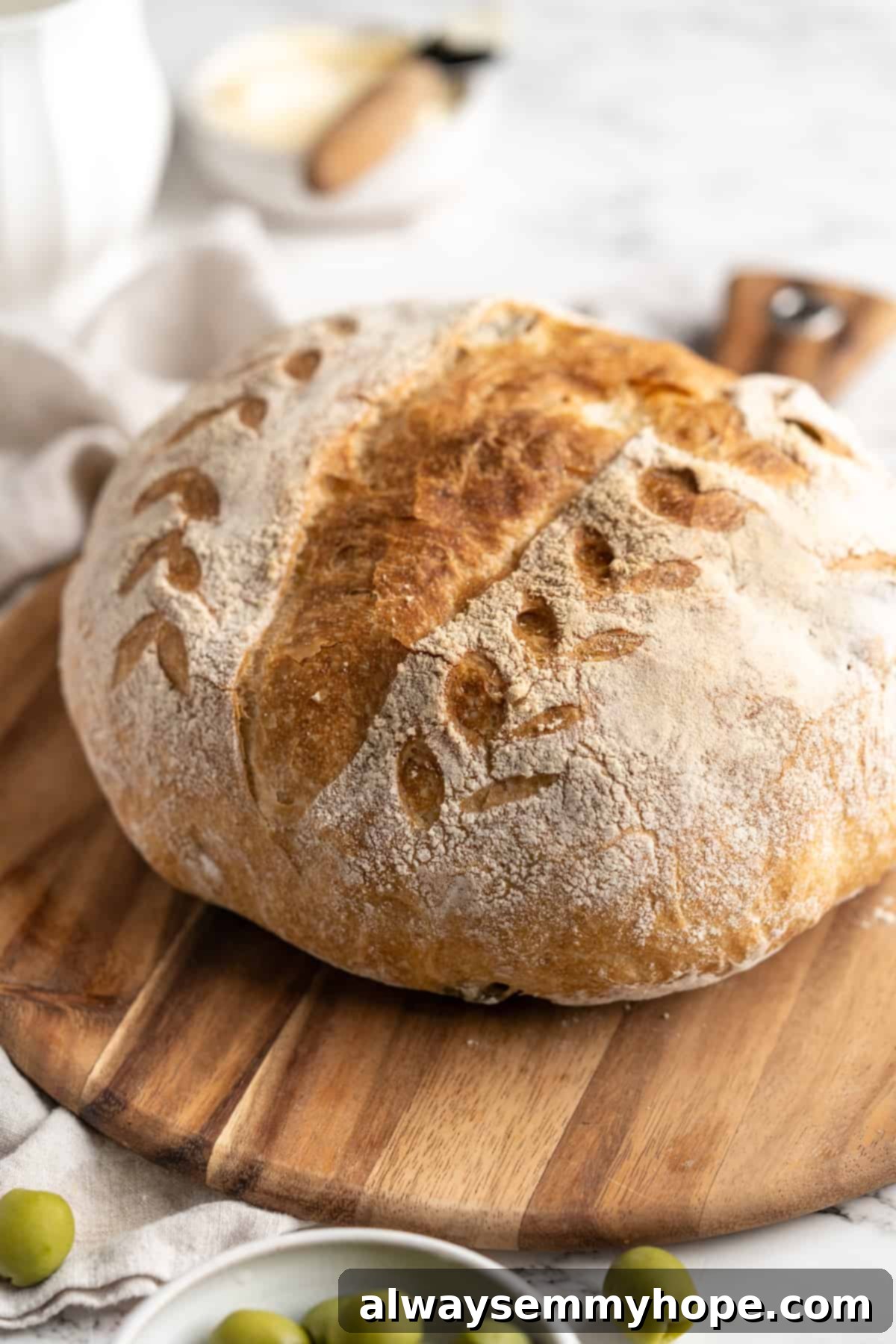 This crusty no-knead olive bread recipe is perfect for beginning bakers, but seasoned pros will love it too. Easy and delicious! Whole olive bread loaf on a rustic wood board, ready to be sliced