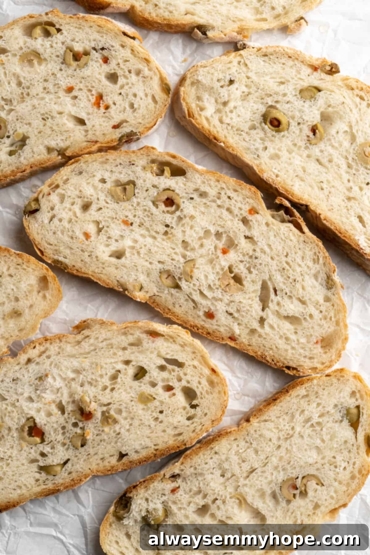This crusty no-knead olive bread recipe is perfect for beginning bakers, but seasoned pros will love it too. Easy and delicious! Overhead view of perfectly sliced olive bread, arranged to showcase its texture and olive distribution