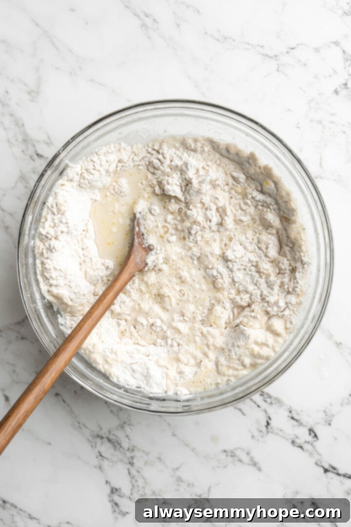 This crusty no-knead olive bread recipe is perfect for beginning bakers, but seasoned pros will love it too. Easy and delicious! Overhead view of wooden spoon stirring wet and dry ingredients together for bread dough in a large bowl