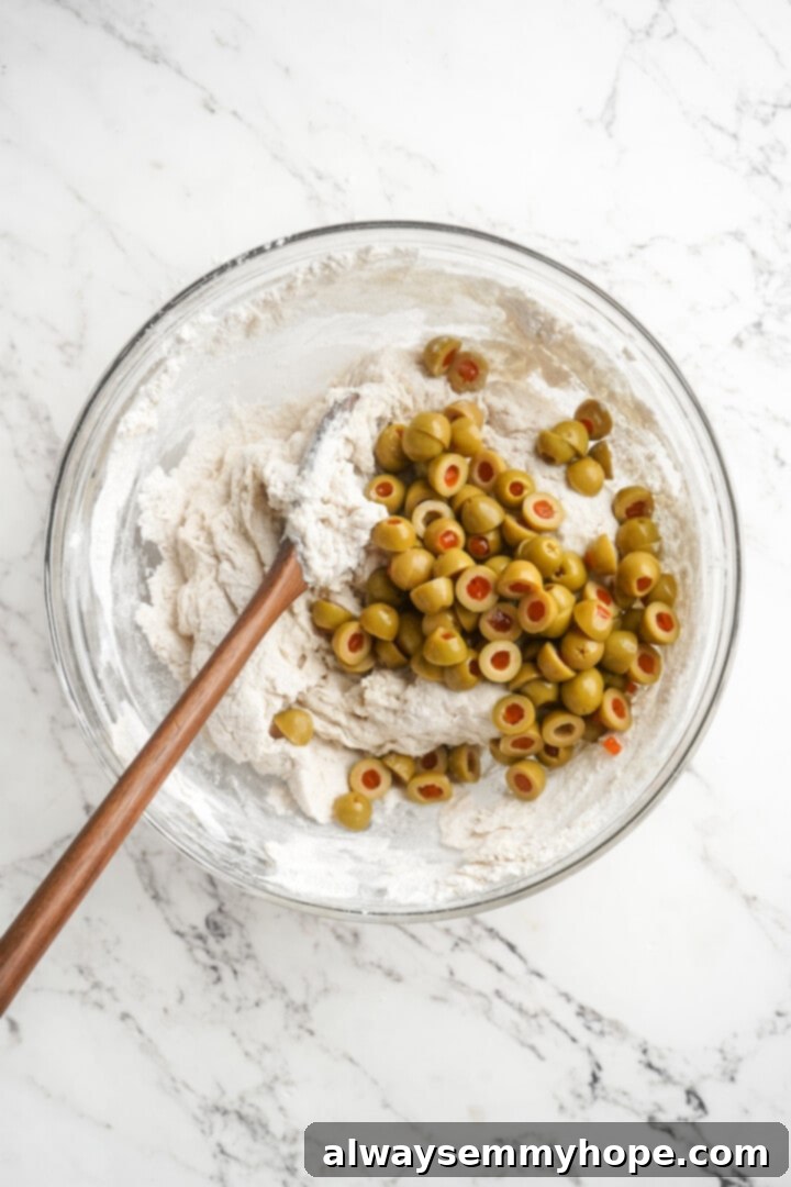 This crusty no-knead olive bread recipe is perfect for beginning bakers, but seasoned pros will love it too. Easy and delicious! Stirring pitted olives into the shaggy bread dough with a wooden spoon