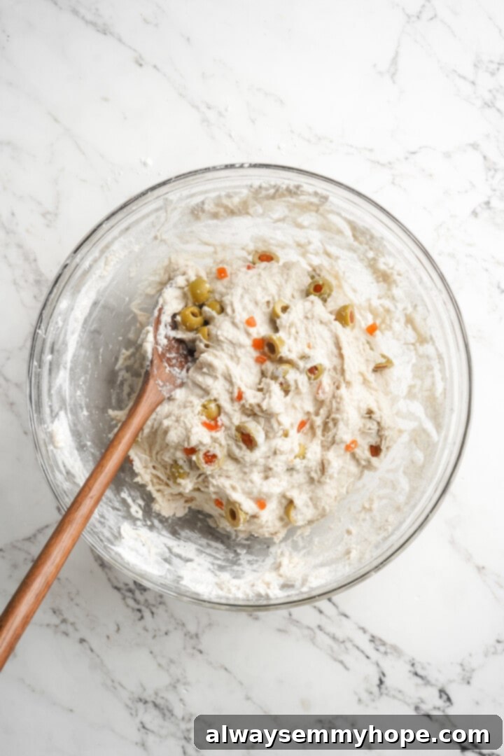 This crusty no-knead olive bread recipe is perfect for beginning bakers, but seasoned pros will love it too. Easy and delicious! Wooden spoon stirring the olive bread dough until all ingredients are well combined