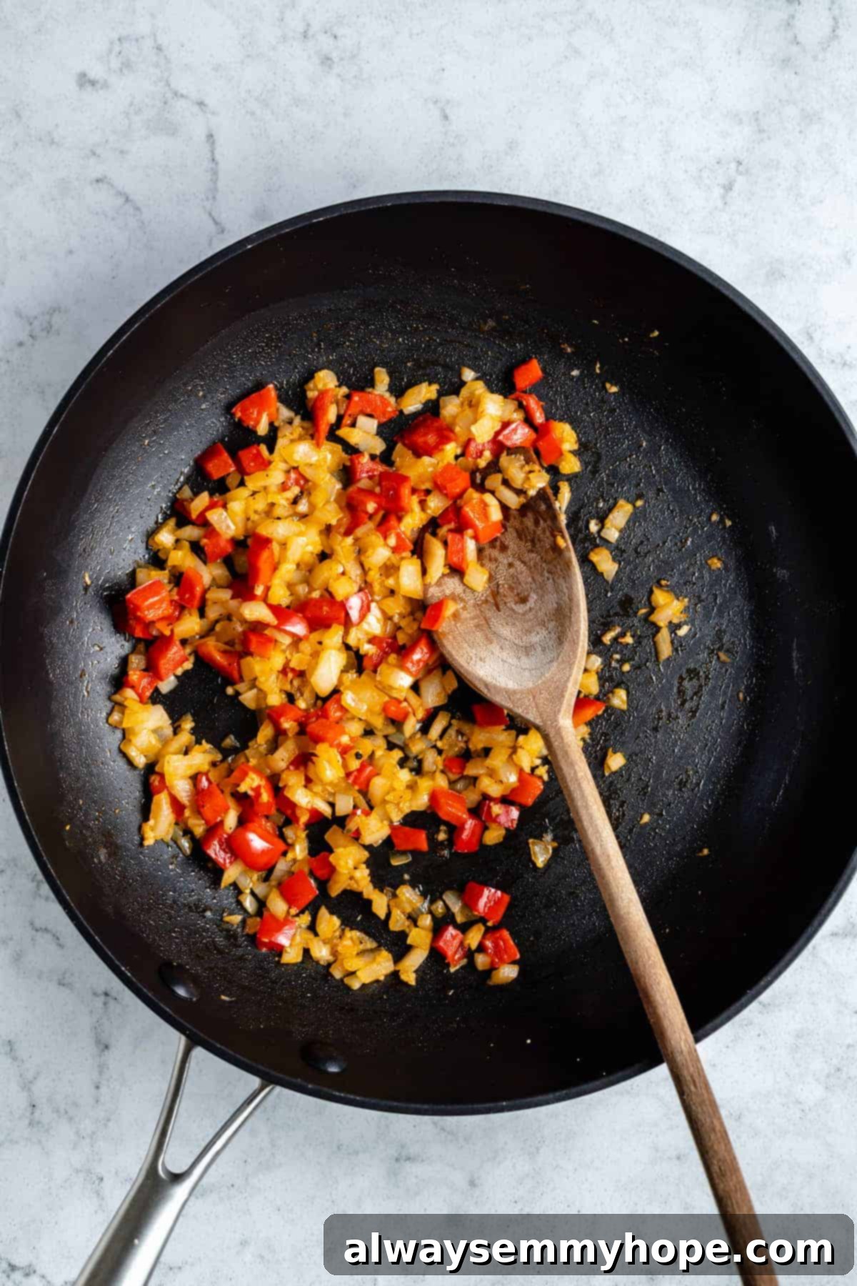 Black bean burgers are made with cooked quinoa, sautéed onions, and smoky strawberry BBQ sauce! Veggie burgers have never tasted this good! Red bell pepper and onion in a pan.