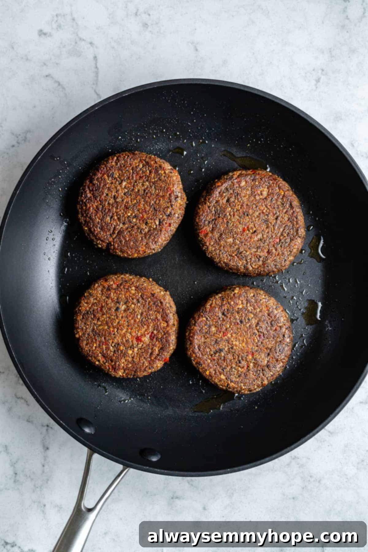 Black bean burgers are made with cooked quinoa, sautéed onions, and smoky strawberry BBQ sauce! Veggie burgers have never tasted this good! Black bean burgers in a pan.