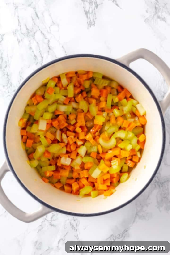 Hearty vegan cheeseburger soup is the ultimate comfort food meal, brimming with savory plant-based flavor and cheesy goodness. It’s like a burger in a bowl! Overhead view of softened carrots, celery, and onions sautéing in a pot with vegan butter