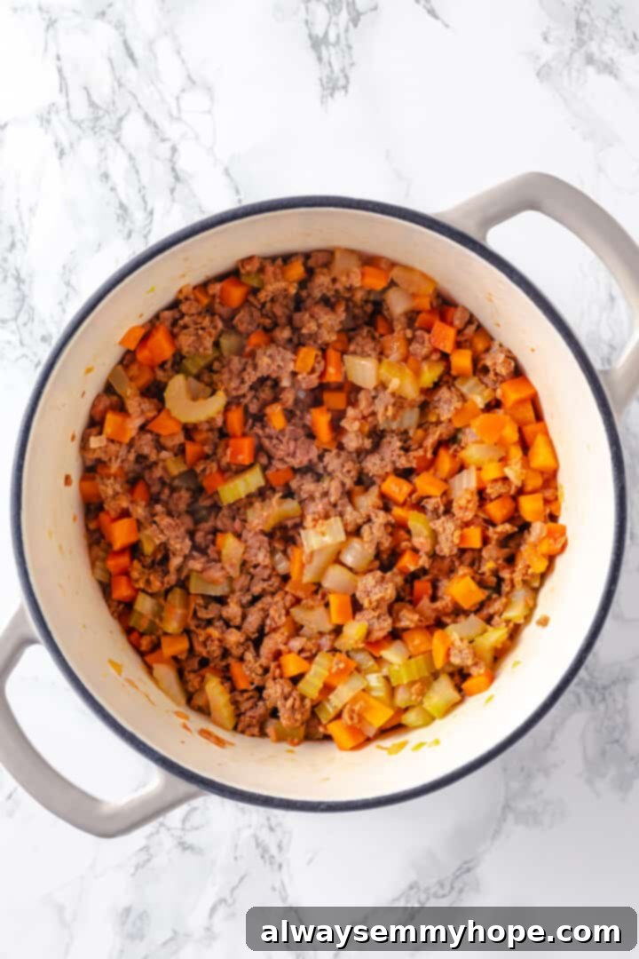 Hearty vegan cheeseburger soup is the ultimate comfort food meal, brimming with savory plant-based flavor and cheesy goodness. It’s like a burger in a bowl! Overhead view of cheeseburger soup with browned vegan meat and vegetables before adding potatoes