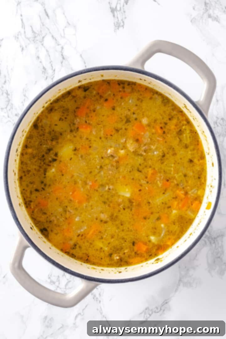 Hearty vegan cheeseburger soup is the ultimate comfort food meal, brimming with savory plant-based flavor and cheesy goodness. It’s like a burger in a bowl! Overhead view of cheeseburger soup in pot before adding vegan cheese, after thickening