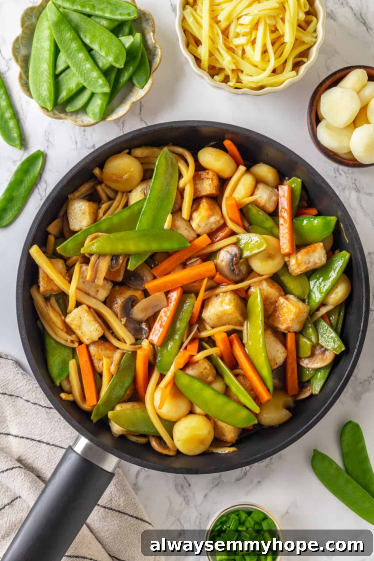 Close-up of a skillet filled with cooked vegan moo goo gai pan, showcasing golden tofu and colorful vegetables