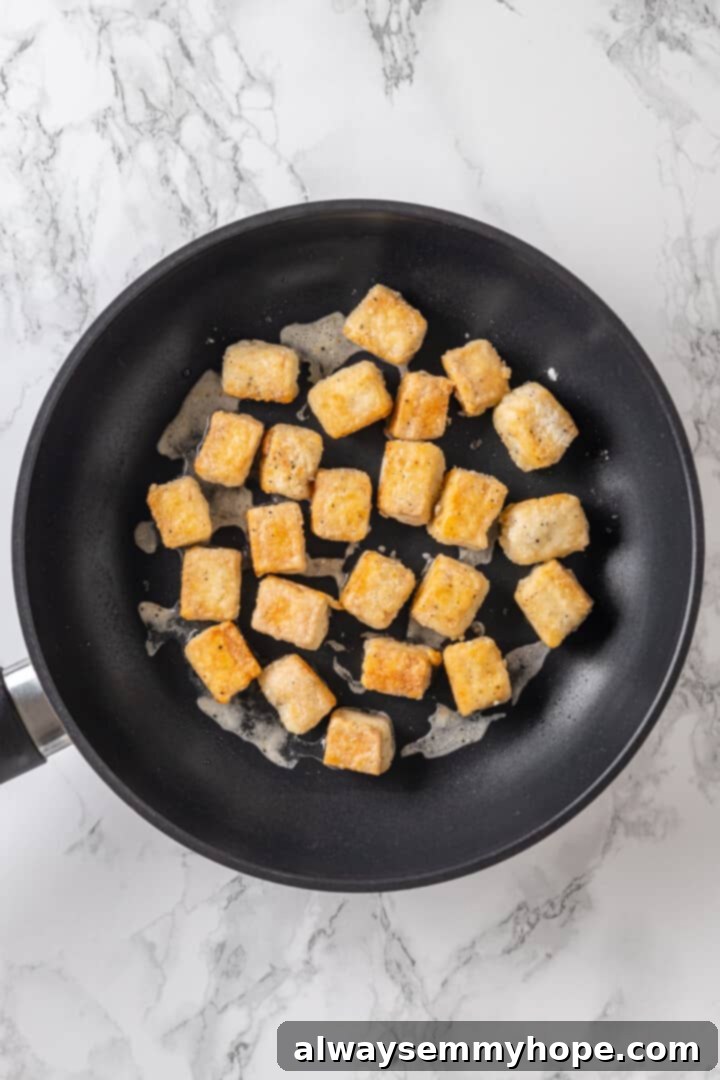 Close-up of tofu cubes cooking and browning in a hot pan with oil