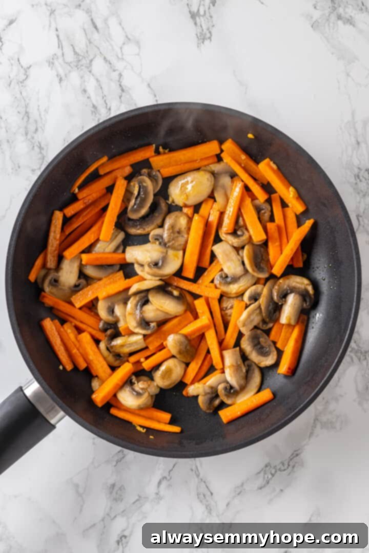 Close-up of sliced mushrooms and matchstick carrots stir-frying in a pan