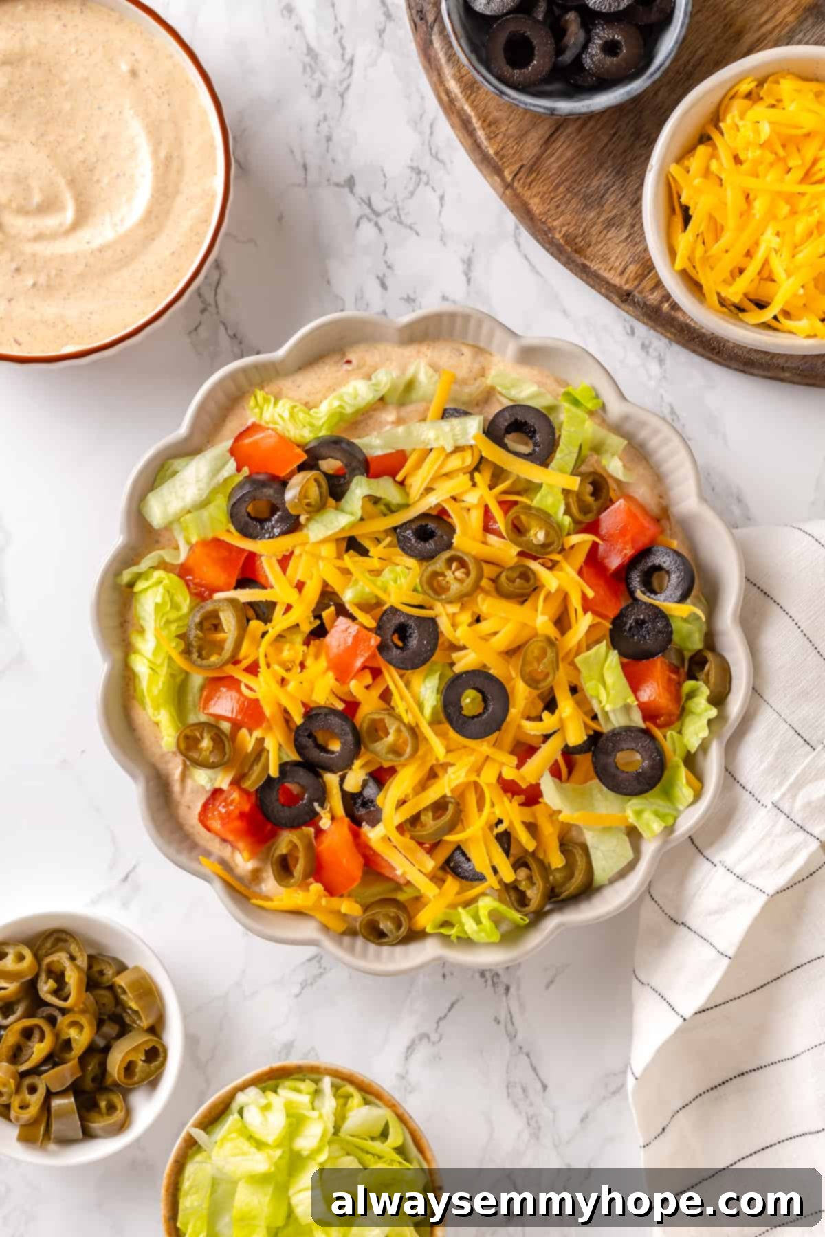 This easy vegan taco dip recipe features a creamy taco-seasoned base topped with lettuce, vegan cheese, tomato, and black olives. It's completely vegan and a perfect party snack! Overhead view of vibrant vegan taco dip in a serving bowl, surrounded by crispy tortilla chips