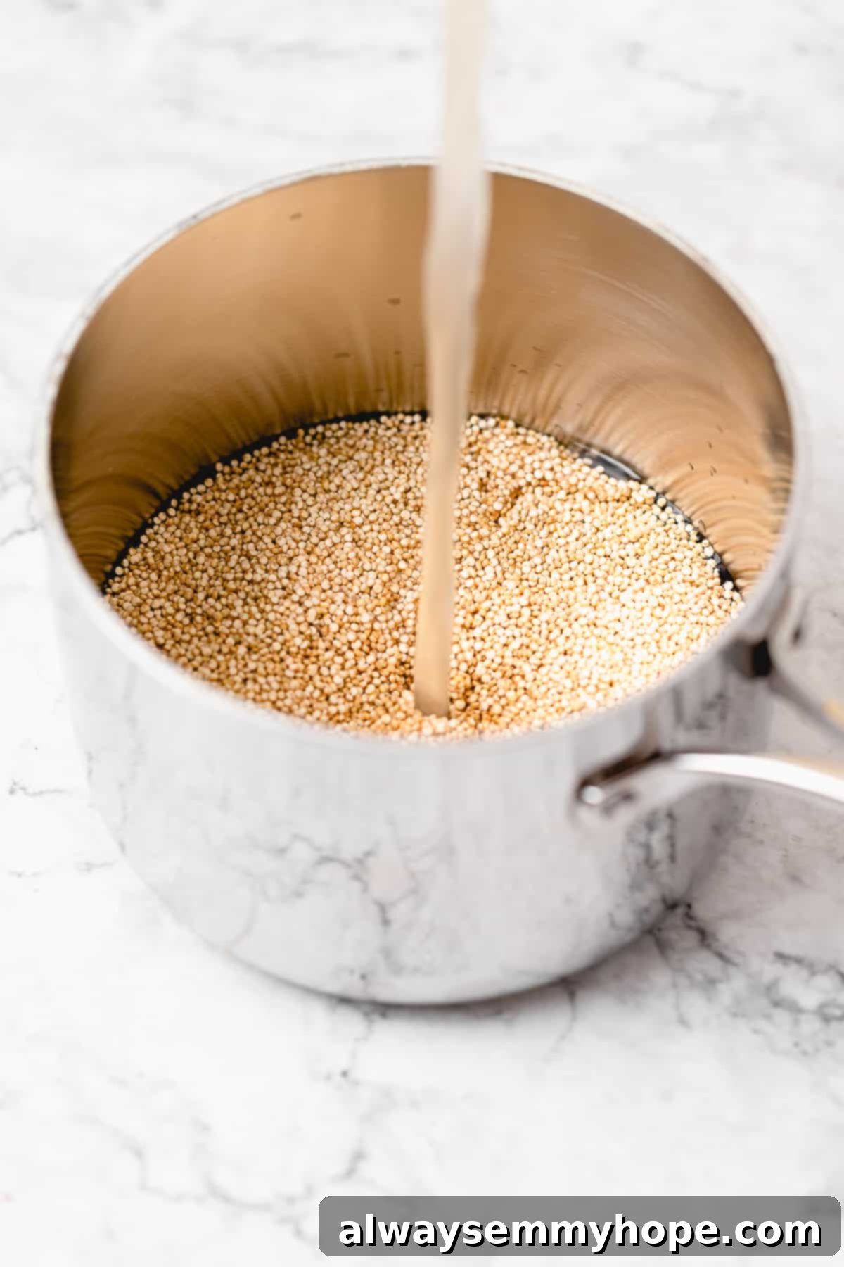 Dry uncooked quinoa in a clear measuring cup, with vegetable broth being poured into a pan to cook the quinoa