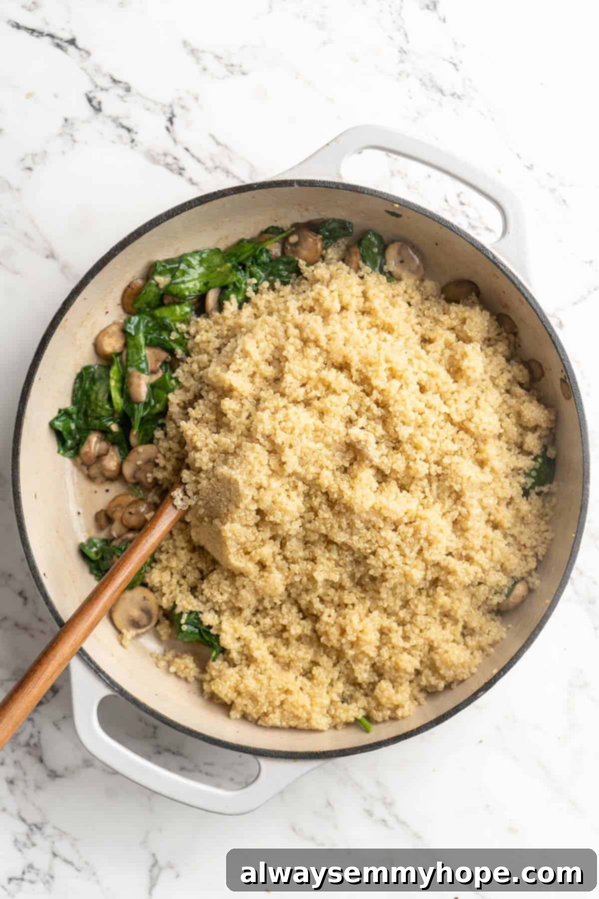 Overhead view of perfectly cooked quinoa being added to a pan of sautéed spinach and mushrooms