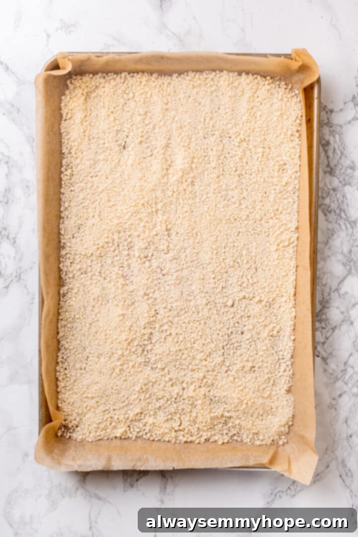 Grated vegan Parmesan cheese spread evenly on a parchment-lined baking sheet. Vegan Parmesan cheese spread on parchment-lined baking sheet