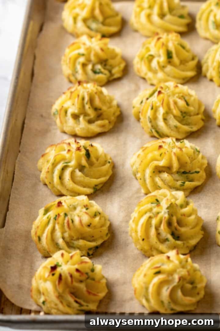 A sheet pan full of freshly baked duchess potatoes, garnished with herbs