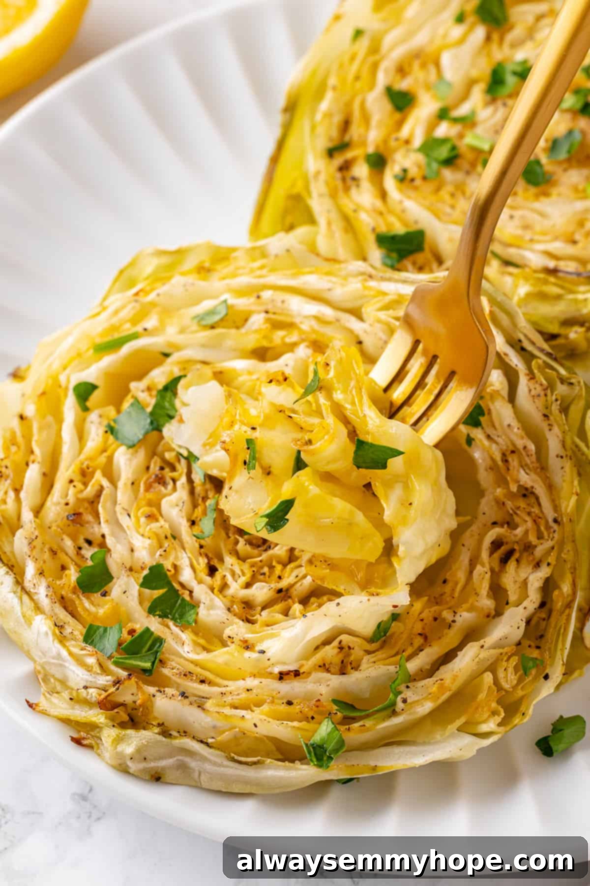 Two golden-brown roasted cabbage steaks on a white plate with a gold fork beside them, ready to be eaten.