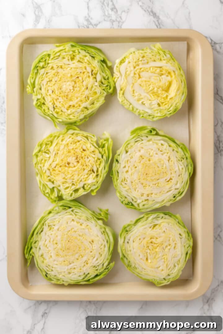 Overhead view of unseasoned cabbage steaks arranged neatly on a parchment-lined baking sheet.