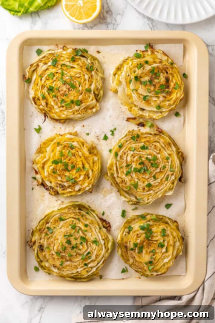 Overhead view of finished roasted cabbage steaks on a baking sheet, drizzled with lemon juice and garnished with fresh parsley.