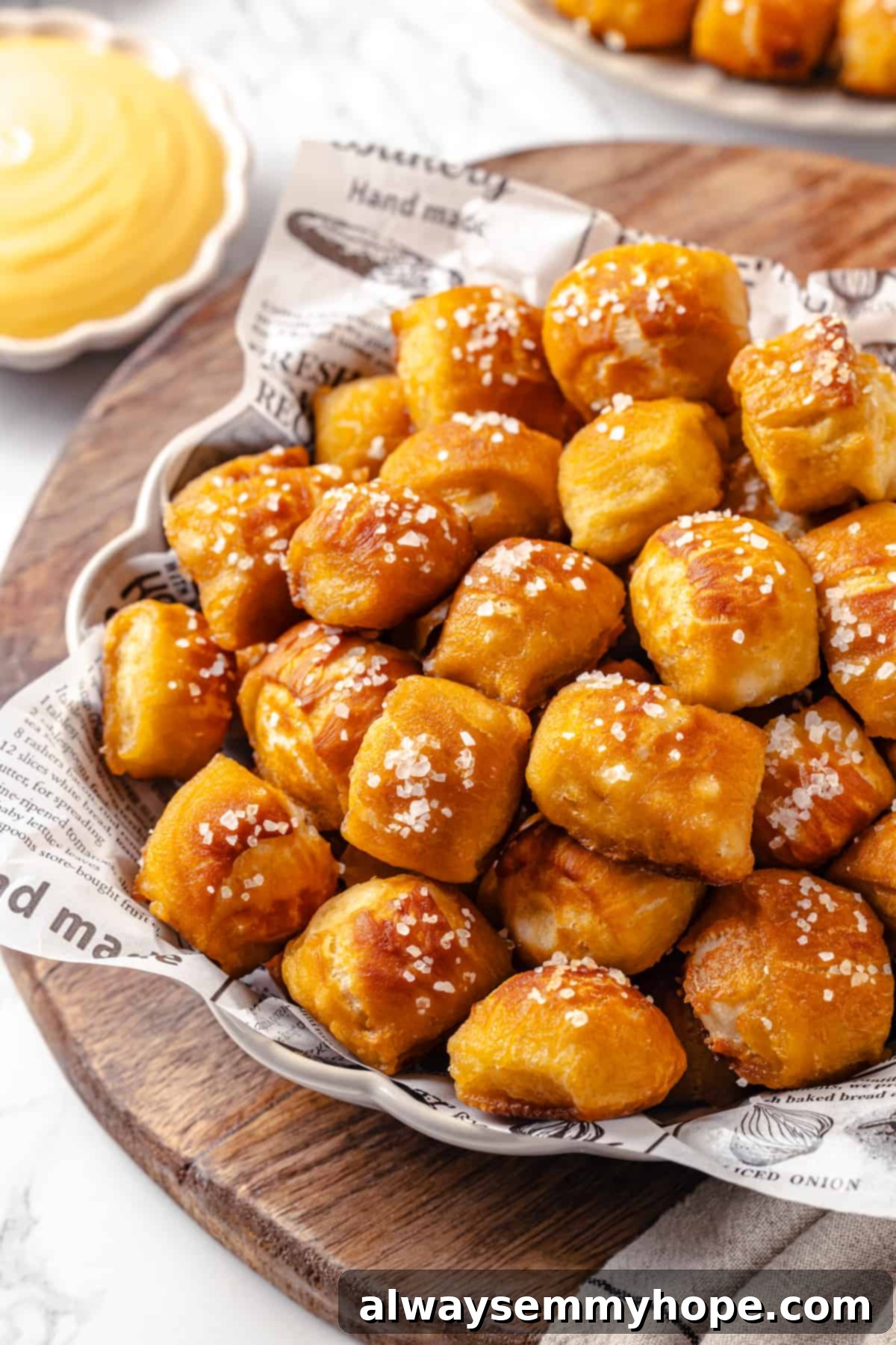 Homemade vegan pretzel bites are the snackable sibling to regular soft pretzels! They're perfect for game day parties and easy to make too. A close-up of a bowl overflowing with vegan pretzel bites, with a creamy vegan cheese dip softly blurred in the background.