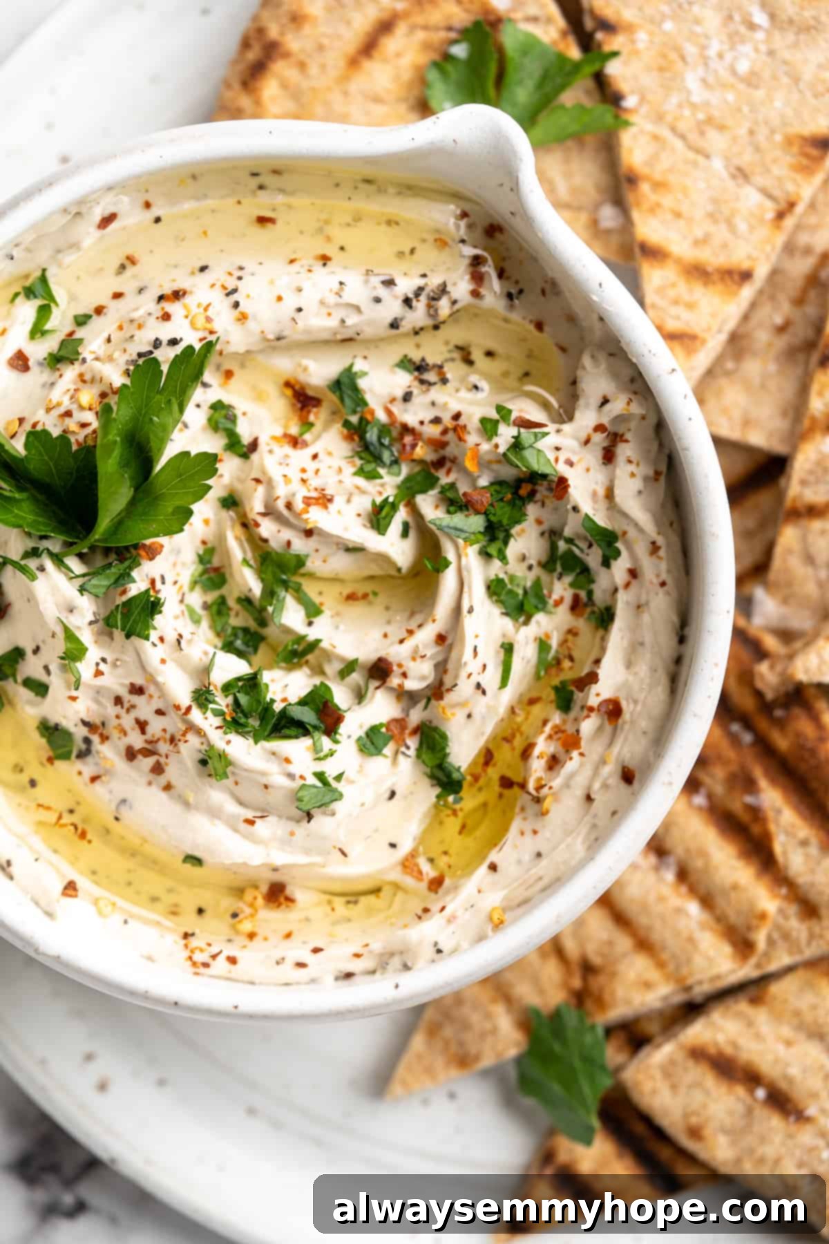 Overhead view of a finished vegan whipped feta dip, elegantly served in a bowl on a platter alongside golden, crispy grilled pita chips.