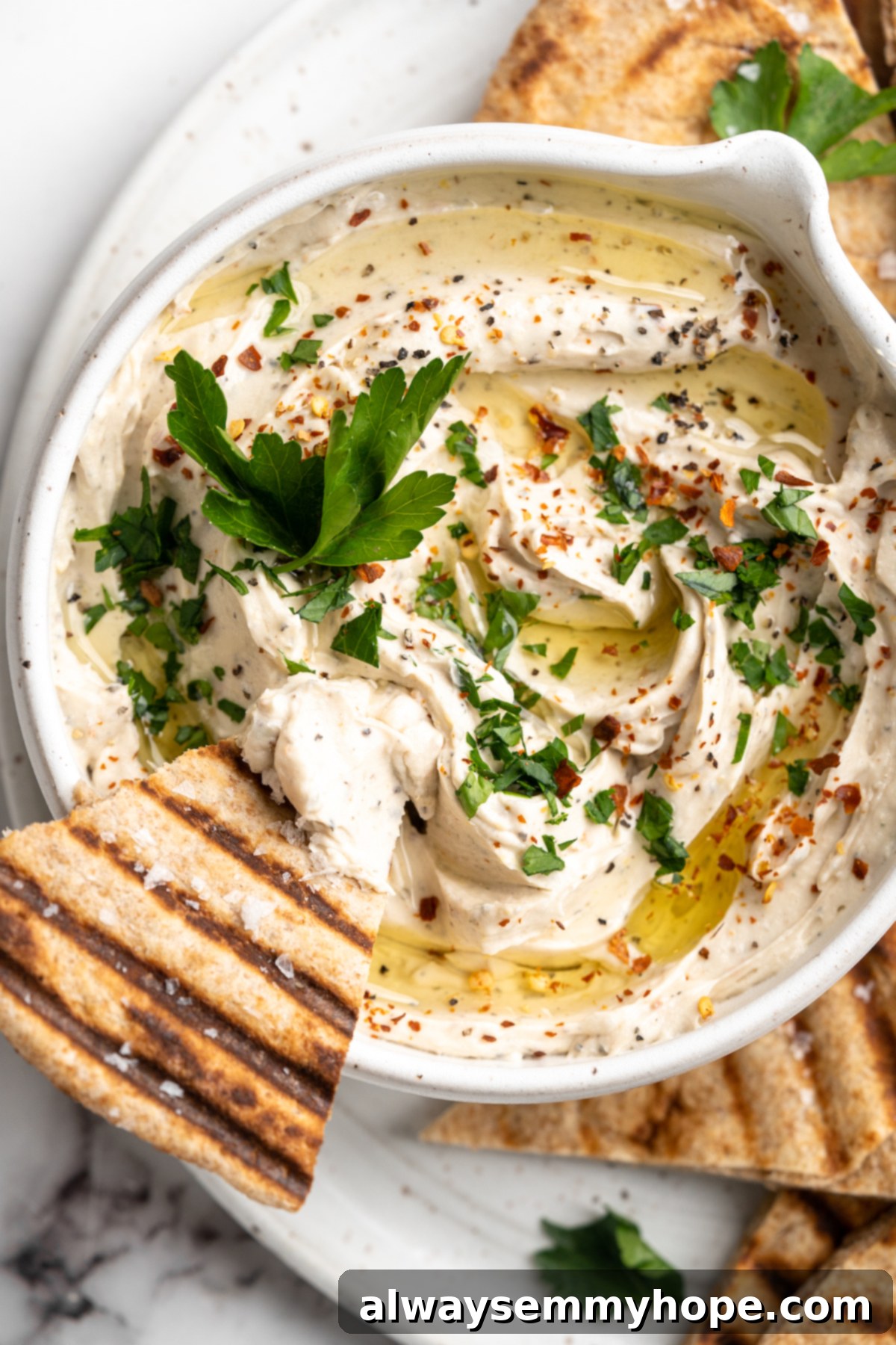 Close-up overhead view of creamy vegan whipped feta dip in a bowl, with a perfectly golden grilled pita chip poised above it, ready for dipping.