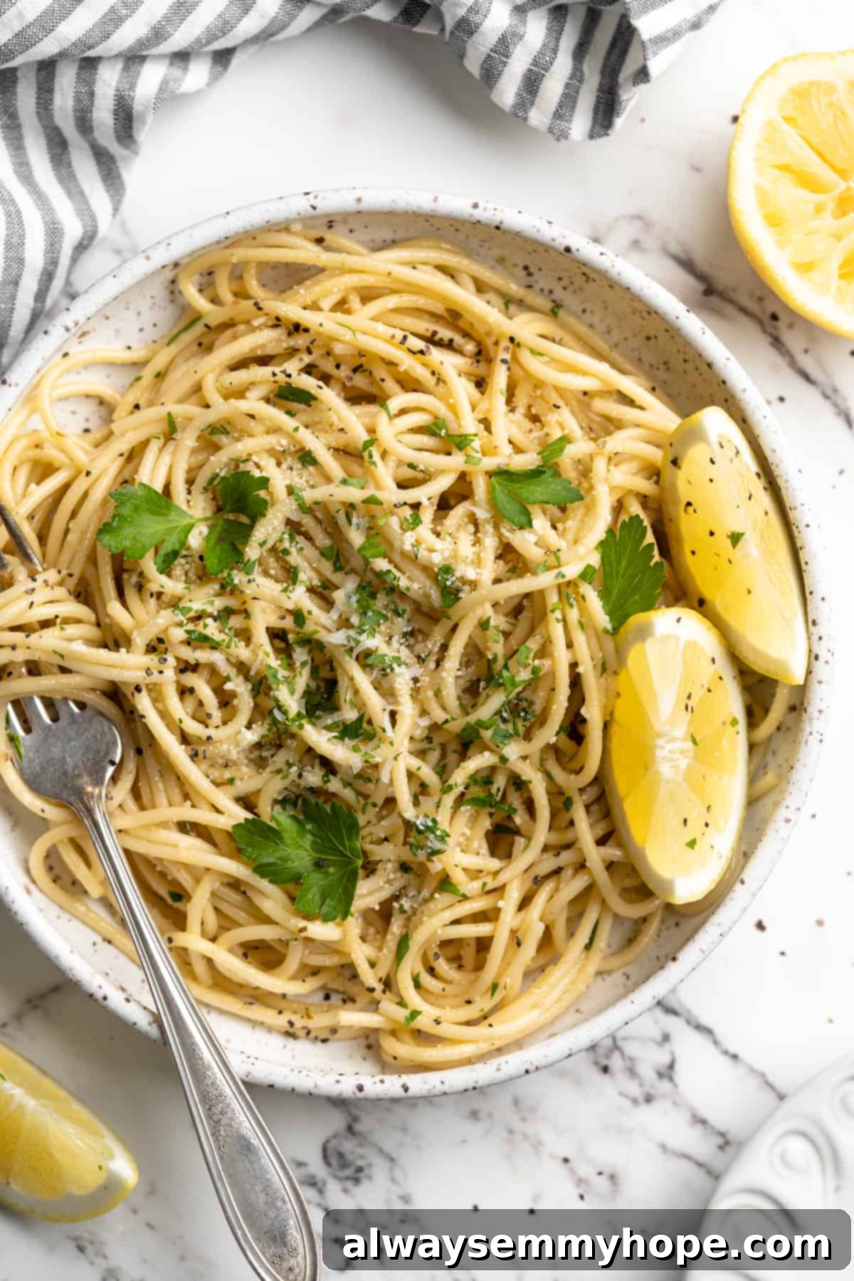 This lemon pasta recipe is light and flavourful, with bright lemon, plenty of garlic, and umami vegan Parmesan. An easy weeknight dinner! Overhead view of lemon pasta on a plate with a fork and fresh lemon wedges, garnished with fresh parsley.