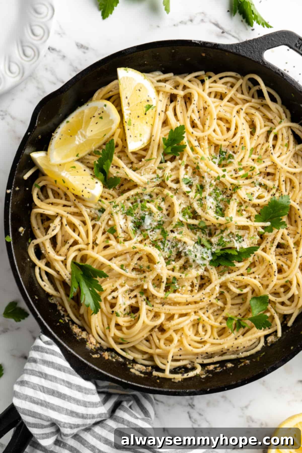This lemon pasta recipe is light and flavourful, with bright lemon, plenty of garlic, and umami vegan Parmesan. An easy weeknight dinner! Overhead view of lemon pasta simmering in a skillet, garnished with fresh lemon wedges and parsley.