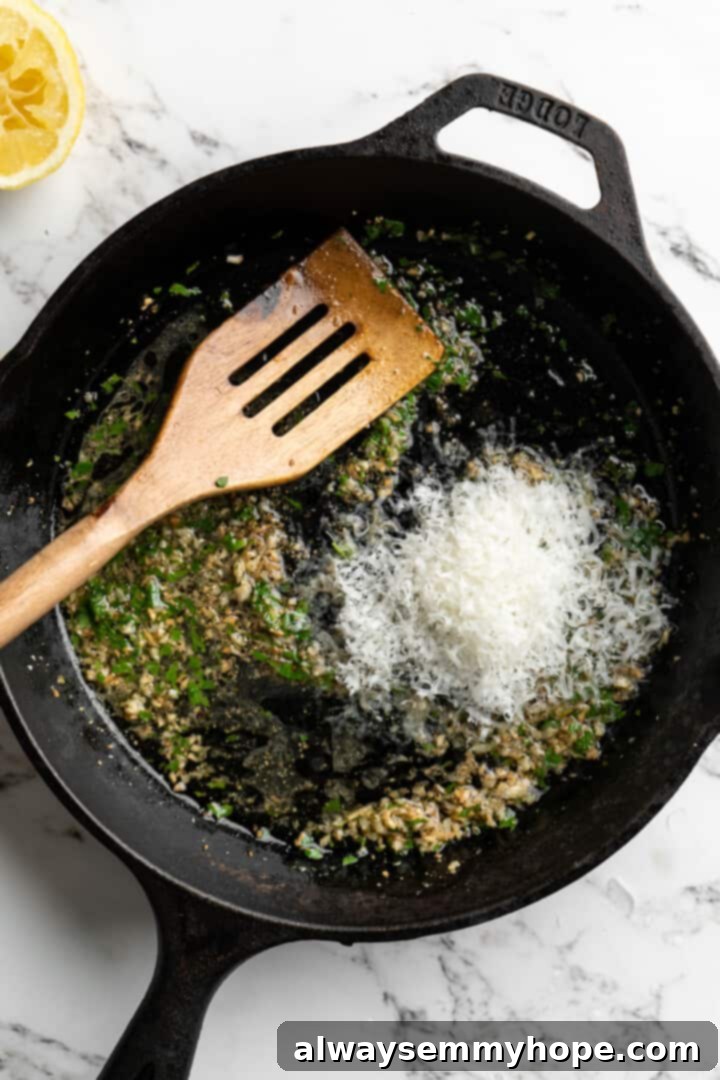 This lemon pasta recipe is light and flavourful, with bright lemon, plenty of garlic, and umami vegan Parmesan. An easy weeknight dinner! Overhead view of vegan Parmesan cheese being added to the simmering lemon garlic sauce in a skillet.