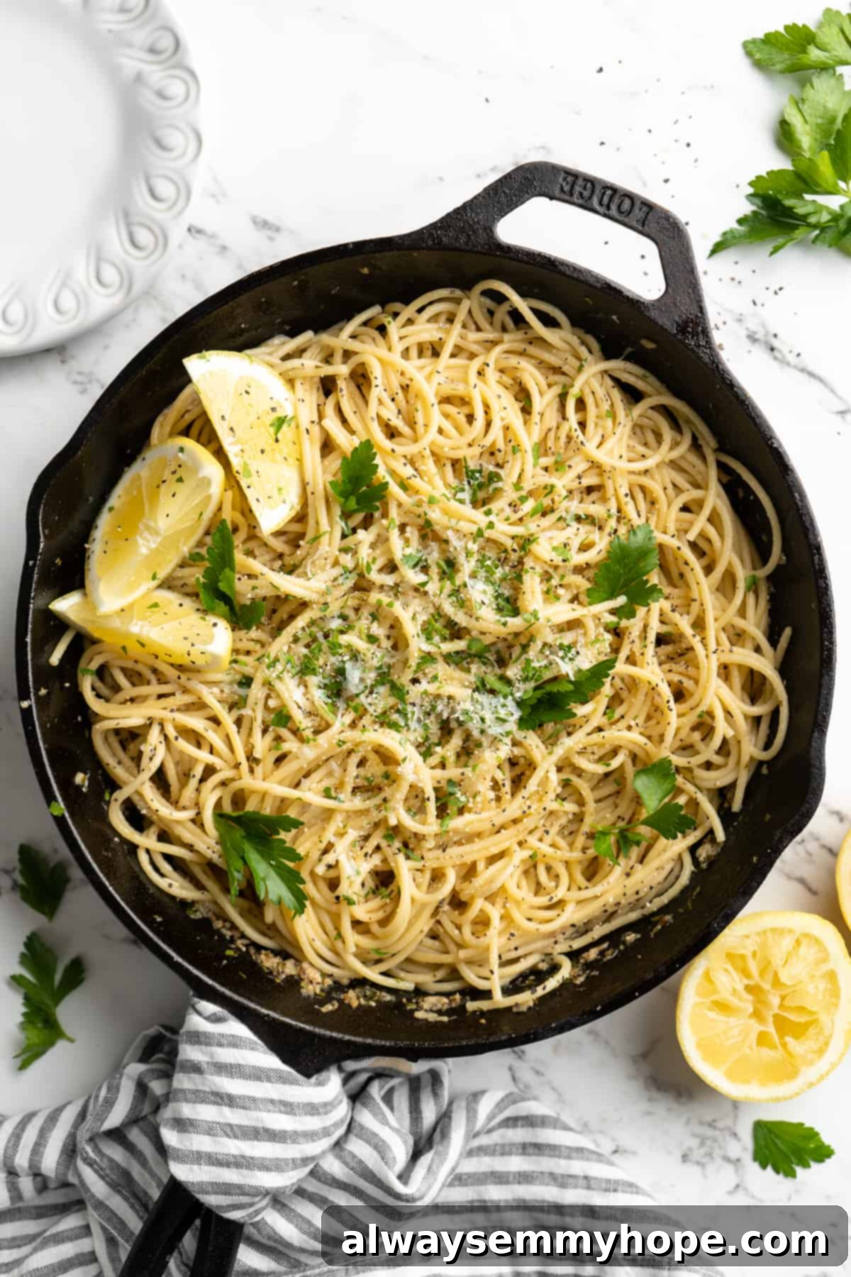 This lemon pasta recipe is light and flavourful, with bright lemon, plenty of garlic, and umami vegan Parmesan. An easy weeknight dinner! Overhead view of finished lemon pasta in a skillet, garnished with fresh lemon wedges and parsley.