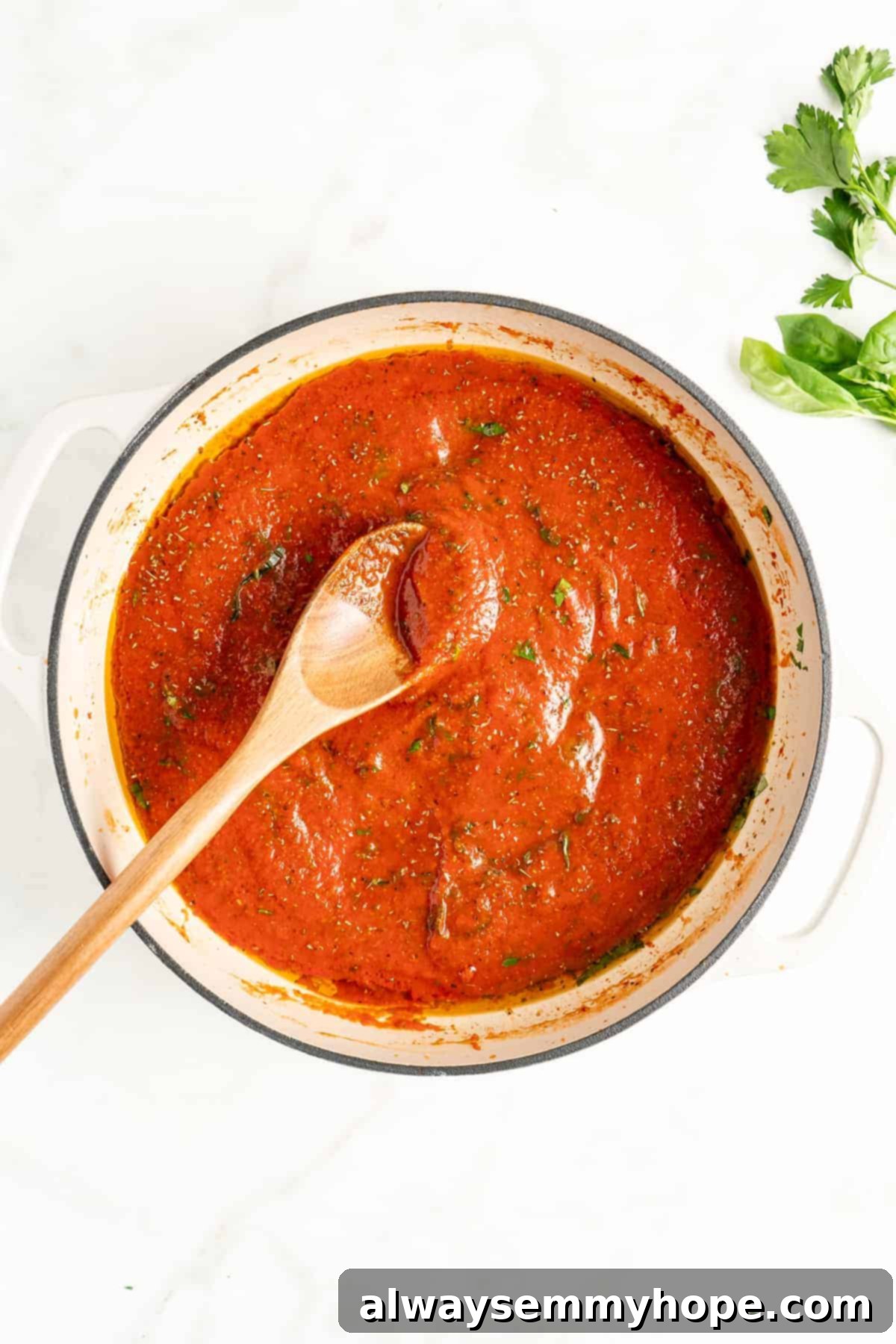You won't believe how easy it is to make homemade marinara sauce! This recipe is ready to eat in 15 minutes. No peeling or chopping tomatoes! Overhead view of homemade marinara sauce simmering gently in a white pot with a wooden spoon.