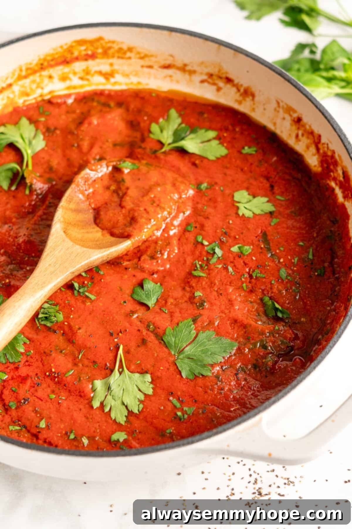 You won't believe how easy it is to make homemade marinara sauce! This recipe is ready to eat in 15 minutes. No peeling or chopping tomatoes! Close-up of freshly made homemade marinara sauce in a white pot with a wooden spoon, ready to serve.