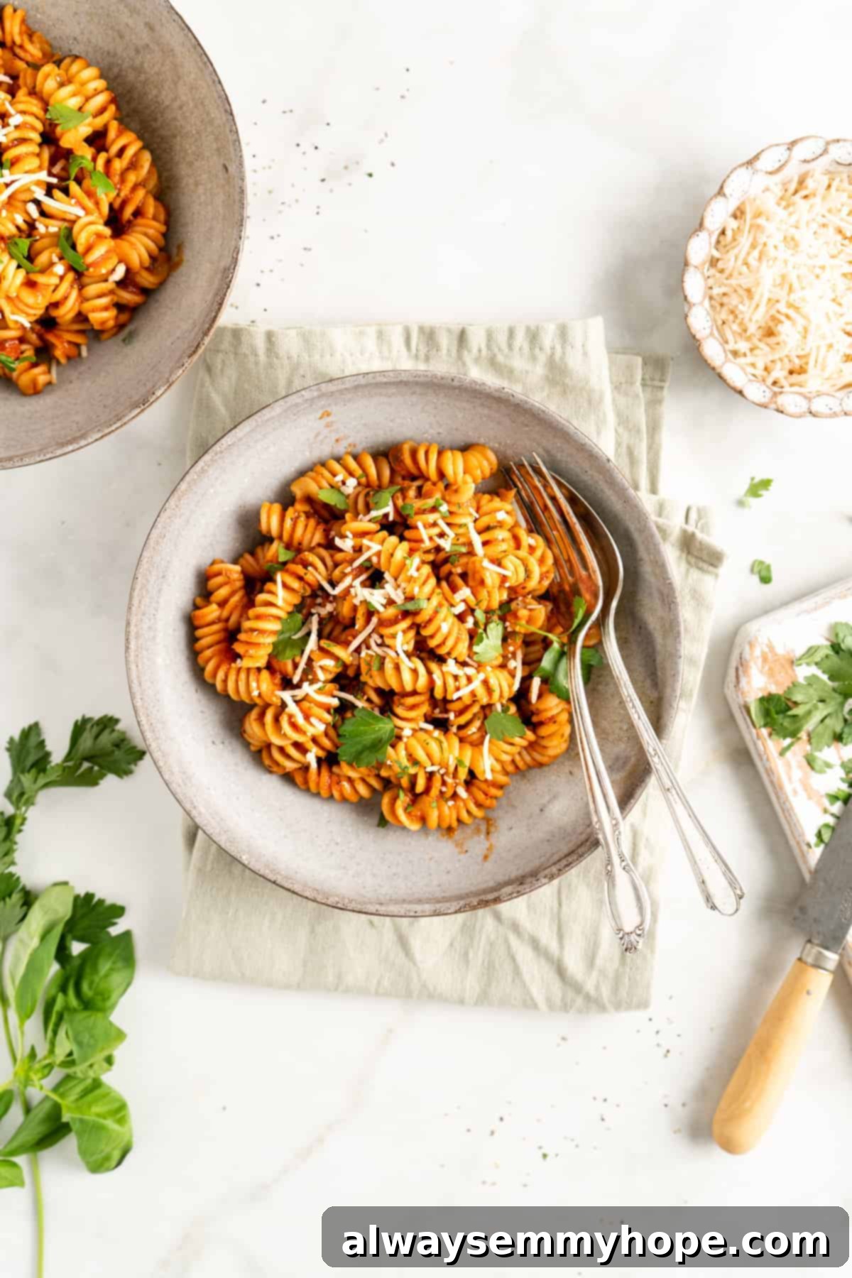 You won't believe how easy it is to make homemade marinara sauce! This recipe is ready to eat in 15 minutes. No peeling or chopping tomatoes! Overhead view of two bowls of rotini pasta with homemade marinara sauce, garnished with Parmesan cheese and fresh parsley.