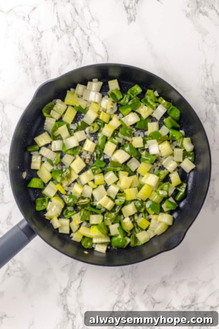Close-up of diced celery, onion, and green bell pepper sautéing in olive oil in a skillet.