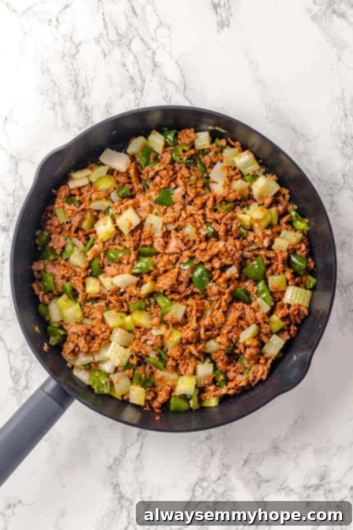 Sautéed vegan sausage and vegetables mixed in a skillet, browning nicely.